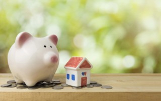 Close-up of a ceramic piggy bank and small house on top of coins. Blurred green background.