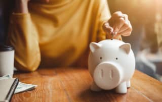 Close-up of woman's hand putting coins into a piggy bank