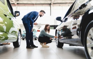 Beautiful young Caucasian female choosing new car, checking its wheels while male salesman helps her
