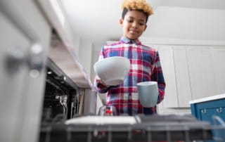 Boy Helping With Chores At Home By Stacking dishes In Dishwasher