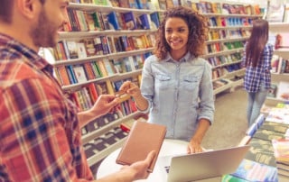 Beautiful afro american girl is smiling while buying book at the bookshop using a credit card