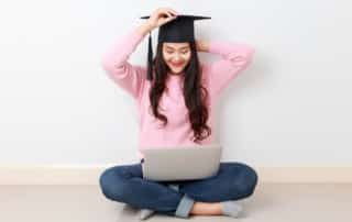 Young woman with graduation cap on looking down at her laptop