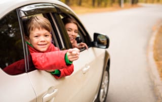 Outside view of a cute smiling boy looking out car window while traveling with parents in autumn forest