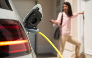 An electric vehicle plugged into a power outlet with a young woman blurred in the background locking the car