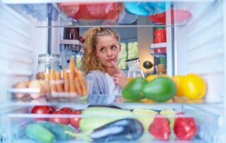 Woman standing in front of fridge full of groceries and taking juice. Picture taken from inside of fridge.
